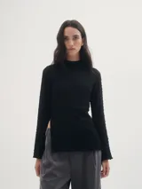 Blusa negra de crepe texturado, con cuello alto, mangas largas acampanadas y corte asimétrico con abertura lateral.