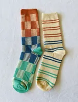 Pack de dos pares de medias de caña media con estampados geométricos. Un par es color ladrillo, azul y verde con diseño de damero. El otro par es color crema con rayas marrones, azules y verdes.