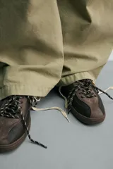 Zapatilla deportiva de estilo retro, confeccionada en una combinación de piezas de cuero texturizado y gamuza en tonos marrones. Presenta un diseño de doble cordonera con cordones claros y suela de goma a tono.