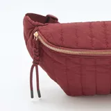 Riñonera color borgoña con diseño acolchado, cierre dorado y correa ajustable.