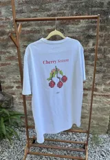 Remera de algodón premium con efecto lavado, manga corta y cuello redondo. Presenta un estampado gráfico en la espalda con el texto 'Cherry Season' y un diseño de cerezas pixeladas.