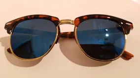 Lentes de sol con montura estilo clubmaster, con marco superior de carey y marco inferior y patillas doradas. Lentes espejados azules.