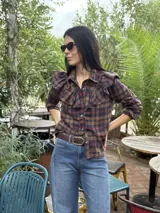 Camisa blanca de algodón con cuello clásico, cierre frontal de botones y detalle de volados en la parte delantera que se extienden hacia los hombros.