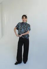 Blusa de seda con estampado floral en tonos marrón y celeste, con cuello alto, manga corta japonesa y cierre cruzado con botones negros visibles en diagonal.
