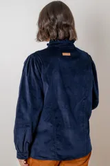 Camisa de pana color verde oliva, con cuello alto con volados, cierre frontal de botones y mangas largas con puños.