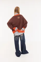 Sweater oversize de corte boxy, color crema con rayas verticales en tonos marrones y detalles de flecos colgantes. Presenta cuello redondo y puños y ruedo en tejido acanalado de color marrón oscuro.