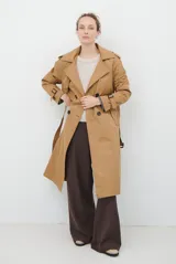 Trench coat color beige con cuello de solapa, cierre frontal abotonado, bolsillos laterales y mangas largas con cintas ajustables. Incluye capucha desmontable y forro interior rayado. La tela exterior cuenta con protección repelente a la lluvia y manchas.