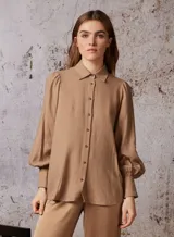 Camisa color beige de lino con cuello clásico, abotonada al frente, mangas largas abullonadas con puños elásticos y corte holgado.