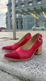 Zapatos de tacón ancho estilo salón, color rojo, con punta fina. Combinan distintas texturas de cuero con grabado tipo cocodrilo y detalles punteados en la puntera. Poseen taco de madera y tira lateral ajustable con hebilla metálica.