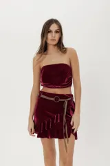 Conjunto de dos piezas de terciopelo color bordó, compuesto por un top strapless con frunces laterales y una minifalda con volados en el borde inferior.