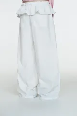 Pantalón blanco de nylon, tiro alto, con cintura elástica y detalle de sobrefalda o peplum superpuesto con hebilla metálica. Corte ancho y pierna recta.