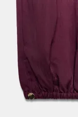 Pantalón bombacho de tiro medio color vino, con cintura ajustable mediante cordón y puños elásticos ajustables con botón en los tobillos.
