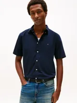 Camisa de manga corta Tommy Hilfiger en color azul marino, confeccionada en tejido popelina con tecnología flex. Presenta cuello clásico, cierre frontal con botones y el logo de la marca bordado en el pecho.
