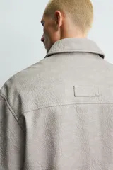 Sobrecamisa de manga corta efecto piel de corte relajado, color gris, con cuello solapa, bolsillo de parche en el pecho y cierre frontal con cremallera.