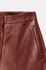 Pantalón de tiro medio confeccionado en 100% piel, con diseño de pierna ancha, cintura con trabillas, bolsillos laterales y cierre frontal con cremallera, botón y ganchos metálicos.