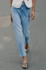Jeans de tiro alto con diseño mom fit, tobilleros, de cinco bolsillos y cierre frontal con cremallera y botón, en color azul claro con efecto deslavado.