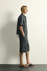 Bermuda cargo relaxed fit confeccionada en denim de mezcla de algodón y lino, con diseño de rayas verticales grises y negras. Cuenta con bolsillos laterales tipo cargo con solapa y cierre frontal con cremallera y botón.