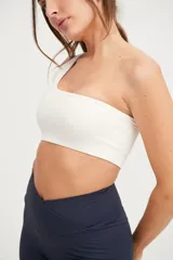 Top deportivo blanco de un solo hombro, con elástico en el contorno superior y sostén interno en el lado derecho.