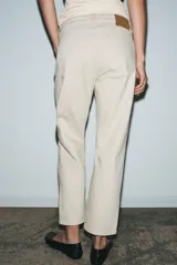 Jeans de tiro medio con corte slim leg, confeccionados en denim color beige. Presentan cintura con trabillas, diseño clásico de cinco bolsillos y cierre frontal con cremallera y botón metálico.