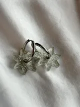 Aros tipo argolla dorada con dije colgante en forma de estrella de acrílico color rosa.