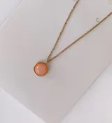 Collar de cadena fina de acero dorado con dije circular de piedra rosada.