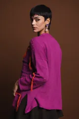 Sweater holgado de punto color fucsia, con cuello redondo, manga larga y detalles de bordados a mano con hilo de lurex y flecos naranjas y negros.