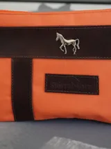 Sobre o cartuchera de lona fucsia con terminaciones y detalles de cuero marrón. Cuenta con cierre superior y aplique metálico de caballo en la parte frontal, además de una etiqueta de cuero con la marca grabada.