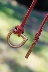 Collar con dije metálico en forma de estribo y tira de cuero color rojo. El dije es de color plateado.