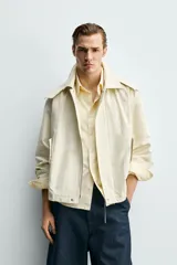 Parka cropped fit de tejido técnico ligero color beige, sin forro interior, con cuello solapa, capucha desmontable y manga larga. Cuenta con bolsillos de solapa en la cadera y cierre frontal con cremallera oculta por solapa con botones a presión.