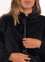 Camisa de pana azul marino con cuello alto, volados en el escote y lazo decorativo. Presenta cierre frontal con botones y mangas largas con puños ajustados.