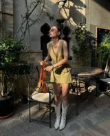 Conjunto de dos piezas color verde oliva con textura arrugada. Incluye un chaleco sin mangas con cierre frontal de lazos y una minifalda ajustada.