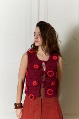 Chaleco tejido en crochet de calce relajado, color bordó con aplicaciones de flores en relieve de color rojo y cierre frontal con lazos.