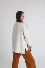 Cárdigan tejido color crudo con cuello en V, cierre con botones y bolsillos frontales con ribete en marrón.