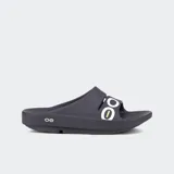 Sandalias de recuperación OOFOS modelo OOahh Sport, color negro con logo blanco en la banda superior. Diseñadas con tecnología OOfoam para una mayor absorción de impactos y soporte ergonómico en el arco del pie.
