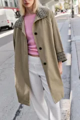 Trench de corte oversize color beige, con cuello alto, cierre frontal de botones y mangas largas con puños vueltos estampados a cuadros. Cuenta con bolsillos delanteros de vivo.