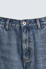Pantalón de jean estilo carpintero con corte relaxed fit, tiro medio y pierna recta. Presenta un lavado azul medio con efecto desgastado y roturas en las rodillas. Incluye bolsillos laterales tipo plastrón, tira multifunción en la pierna, cierre frontal con cremallera y botón.