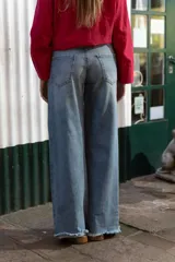 Pantalón de denim tiro alto con corte wide leg, lavado medio con desgastado suave, costuras clásicas y terminación en ruedo deshilachado. Diseño de panel lateral en tono más oscuro.
