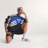 Buzo de cuello redondo Adidas, diseño colorblock en negro, azul eléctrico y blanco. Presenta el logo del Trifolio en dorado en el pecho y las tres franjas blancas sobre fondo negro en las mangas.