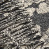 Bufanda de tejido de punto con diseño de estampado animal print en tonos negro y beige, con terminación de flecos en los extremos.