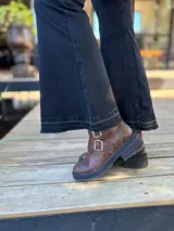 Botas cortas de cuero color marrón con suela track negra. Presentan dos correas ajustables con hebillas metálicas plateadas en el empeine y cierre lateral interno.