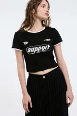 Remera baby blanca de algodón, de corte cropped al cuerpo y mangas cortas. Presenta ribetes negros en contraste en el cuello redondo y los puños, con un estampado localizado de un ají rojo con la inscripción 'Pimentón' en el centro del pecho.