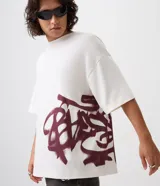 Remera oversized de algodón color blanco, de corte amplio y descontracturado, con cuello redondo, mangas cortas y gran estampa frontal localizada de inspiración urbana en tono bordó.
