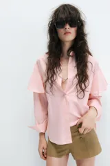 Camisa rosada de cuello solapa y manga larga, con detalle de volantes en las sisas y cierre frontal oculto con botones.