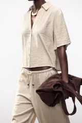 Camisa negra de cuello solapa con escote pico y manga corta. Detalle de nido de abeja en espalda. Cierre frontal con botones.