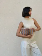 Cartera tipo sobre de cuero trenzado a mano, con diseño de rayas verticales en tonos bordó, amarillo y celeste.