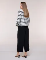 Chaqueta corta de corte estructurado confeccionada en tejido de tweed azul con patrón de cuadros, escote redondo sin solapa, frente abierto, bolsillos falsos y ribetes trenzados con hilos metalizados.
