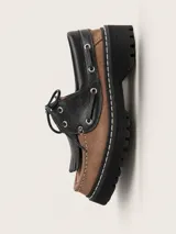 Mocasín de cuero con diseño bicolor en negro y marrón, con detalle de flecos sobre el empeine, cordones y suela track cosida.