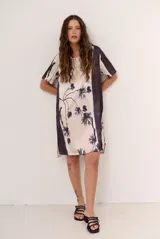Vestido corto de corte recto y holgado, con mangas cortas y cuello redondo. Presenta un diseño estampado con motivos florales oscuros y una franja lateral en tono contrastante.
