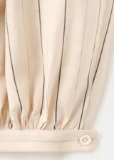 Pantalón balloon de tiro medio en color beige con estampado de rayas finas verticales oscuras. Presenta diseño abombado con bajo ajustable mediante botón.