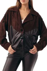Campera bomber de cuero ovino negro combinada con gamuza chocolate, cuello solapa y cierre frontal de botones. Presenta mangas largas con detalles de costuras decorativas y bolsillos laterales ribeteados.
